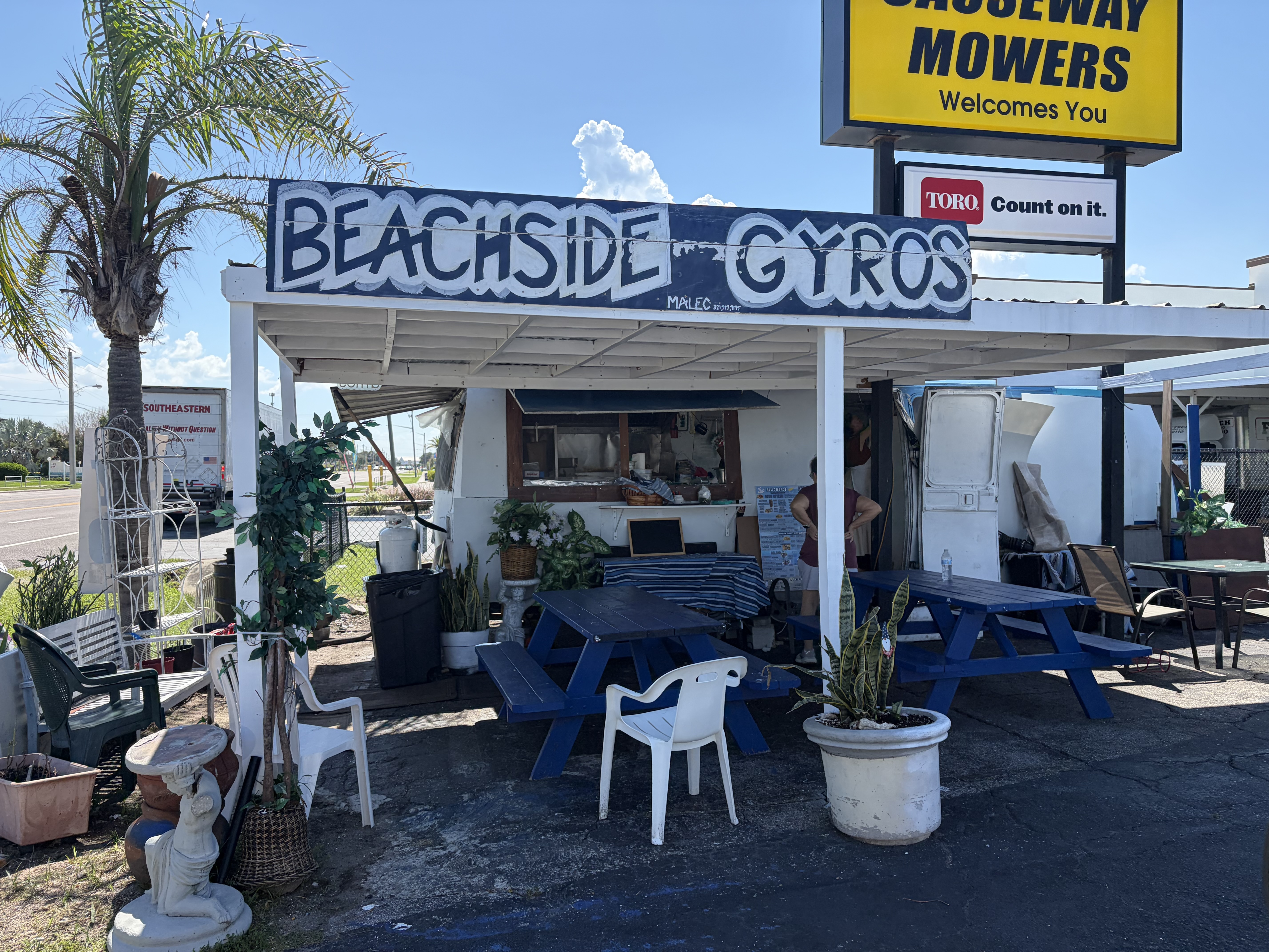 The hand-painted BEACHSIDE GYROS sign over the covered stand with blue picnic tables at the Eau Gallie Causeway